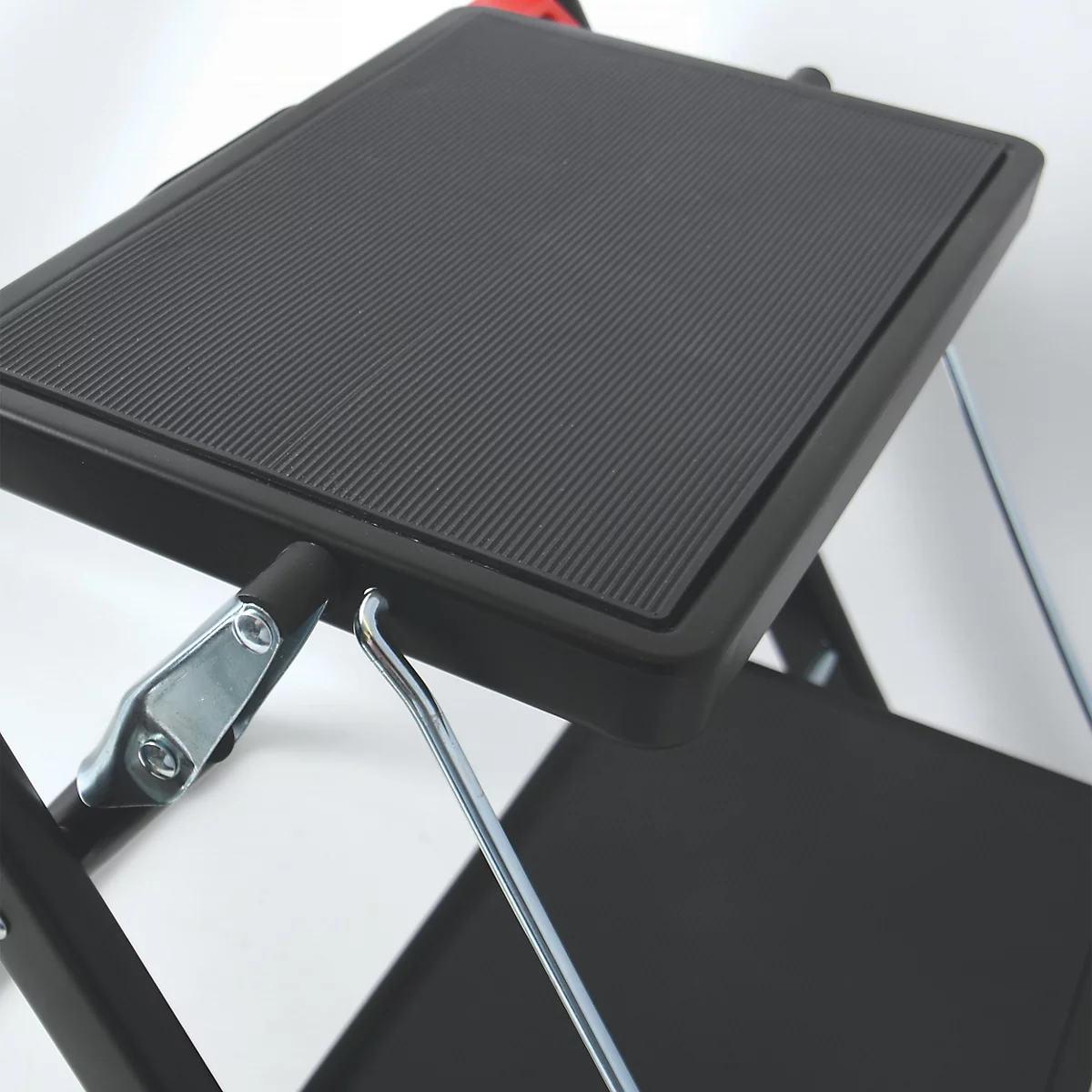 Detailaufnahme einer schwarzen Trittleiter. Die Trittfläche ist geriffelt und mit einer Metallhalterung am Gestell befestigt.