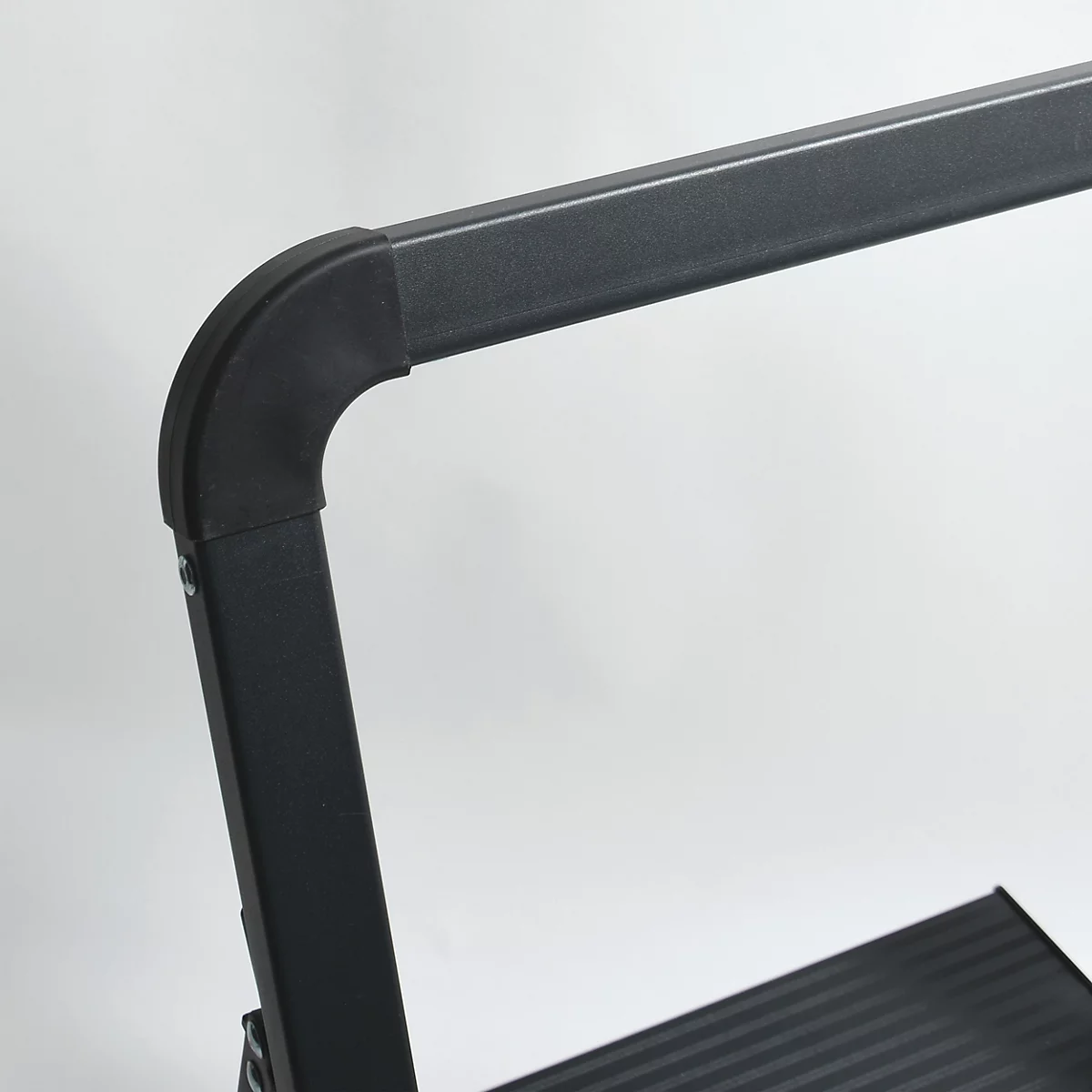 Detailaufnahme einer schwarzen Leiter: Eckverbindung des Handlaufs, gerillte Stufen.