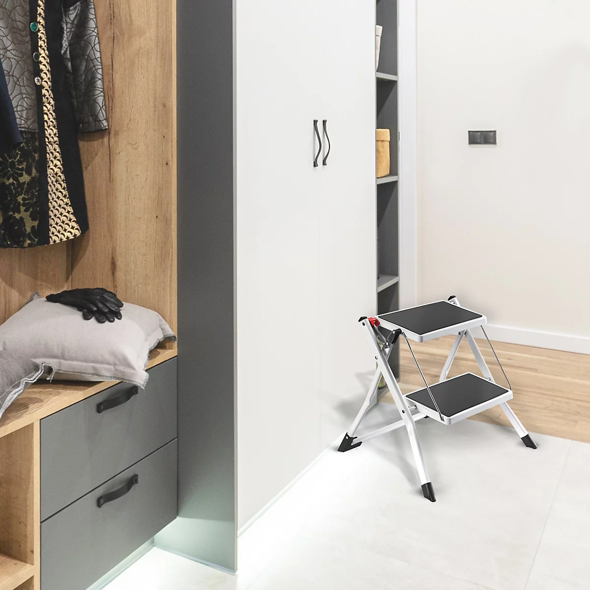 Eine Klapptrittleiter steht in einer Ecke. In der Nähe ist eine Garderobe mit Kleidung.