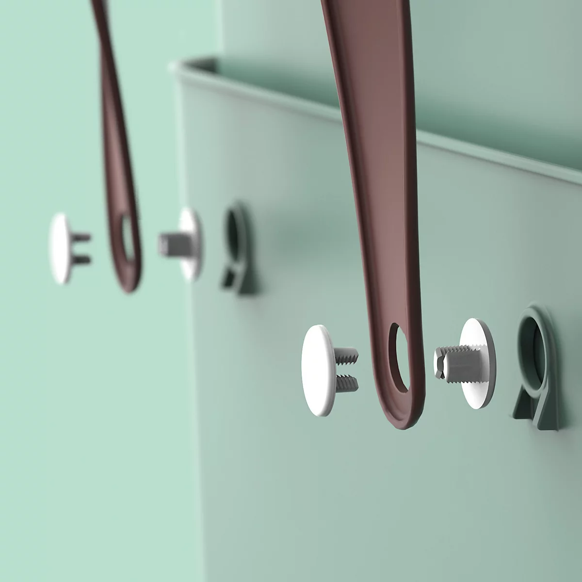 Close-up of wall storage details. Brown leather straps hang on silver pins in a light green wall.