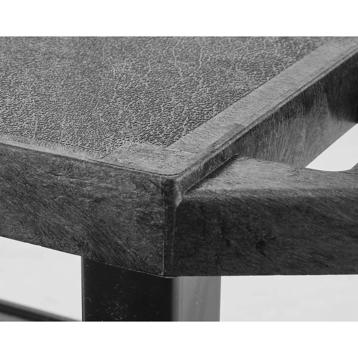 Gedetailleerde close-up van een tafelhoek, getextureerd grijs materiaal, met donkere poten.