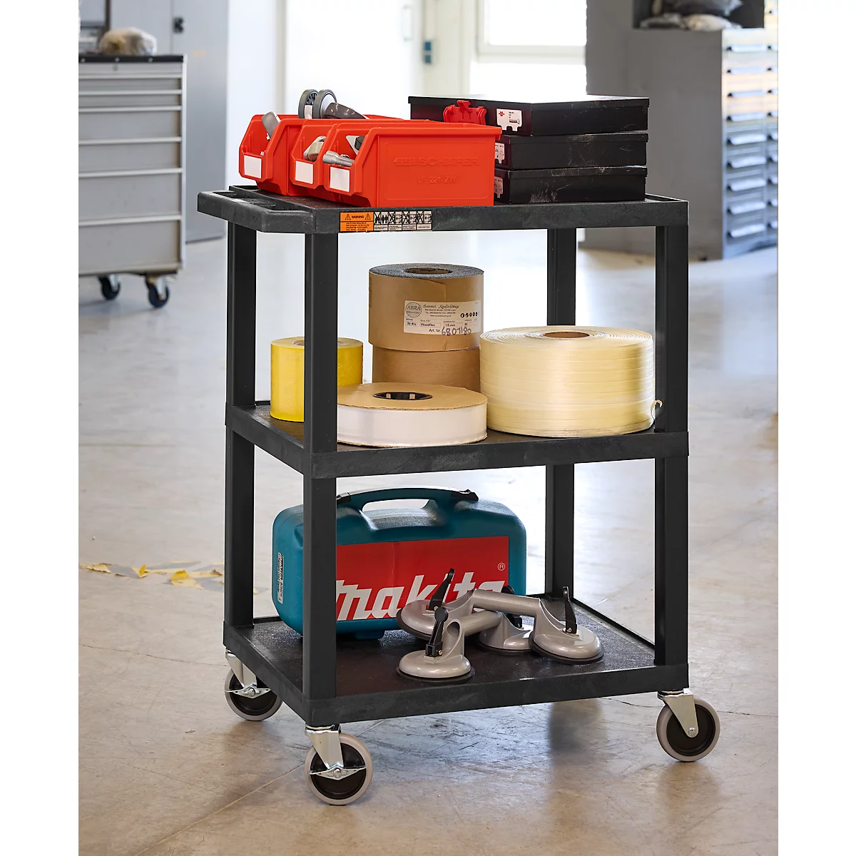 Zwarte gereedschapswagen met gereedschap, rollen tape, containers. In een werkplaats.