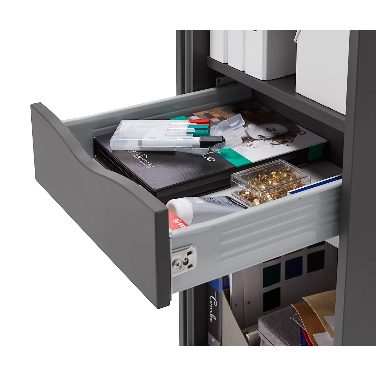 Open lade van een grijze kast met pennen, notitieboekjes en sieraden. Meer laden op de achtergrond.