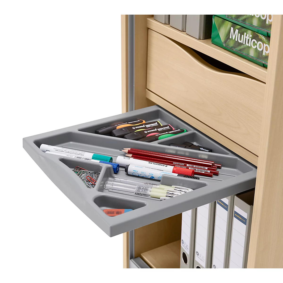 Graue Schublade mit Stiften, Büroklammern und Stiften, teilweise in einem hellen Holzschrank. Dahinter sind Ordner sichtbar.