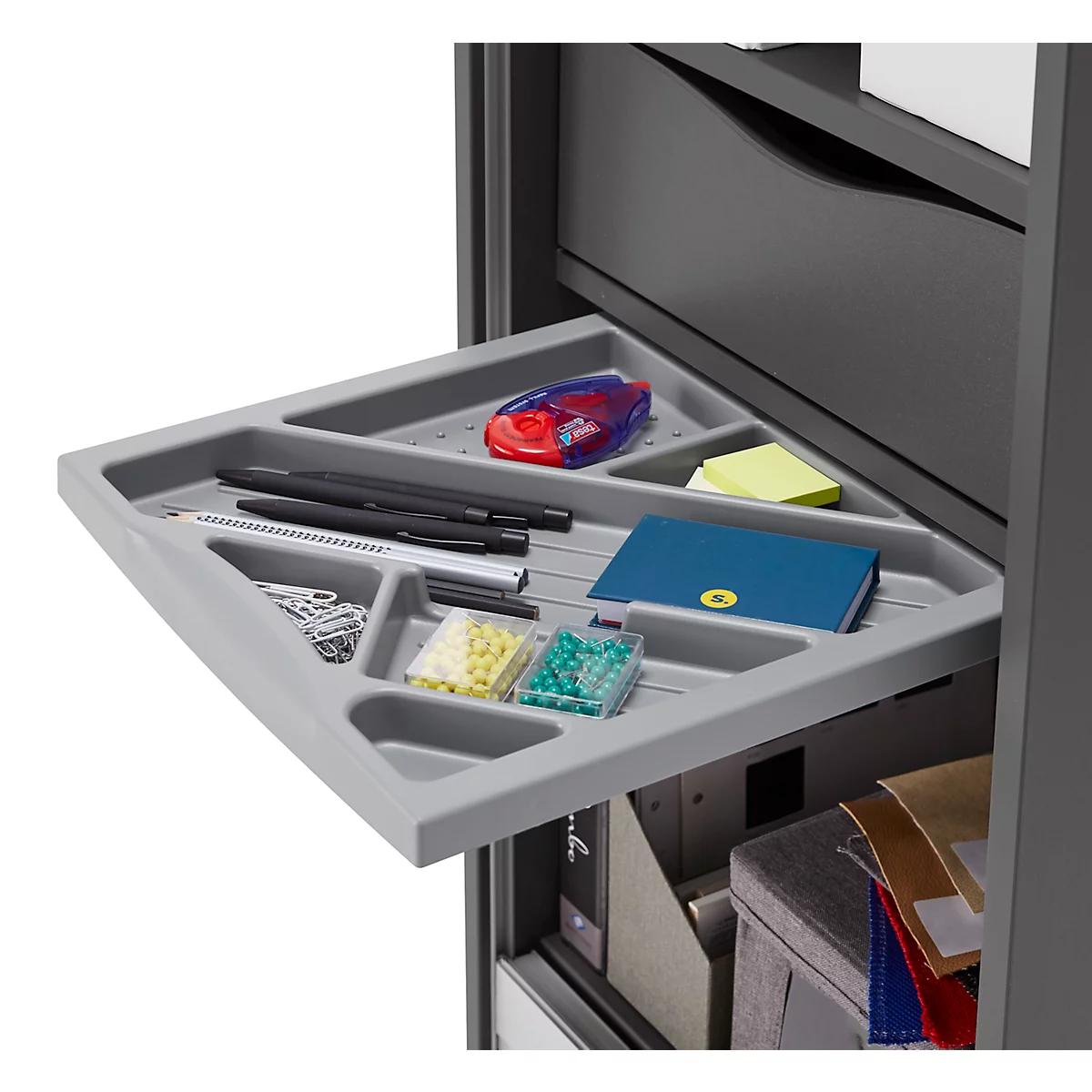 Graue Schublade mit Büromaterial: Stifte, Notizen, Büroklammern, Perlen, Anspitzer und Notizbuch.