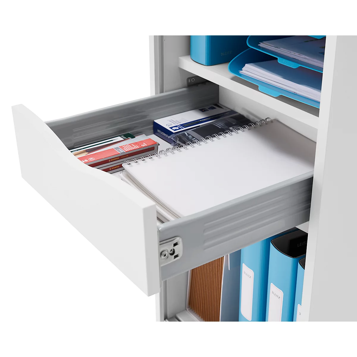 Geöffnete Schublade mit Notizblock, Stiften und Bürobedarf. Der Schrank ist weiß.