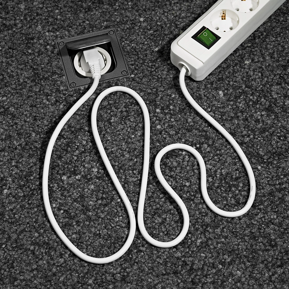 Câble blanc reliant une prise de sol à une multiprise. Le tapis est gris.