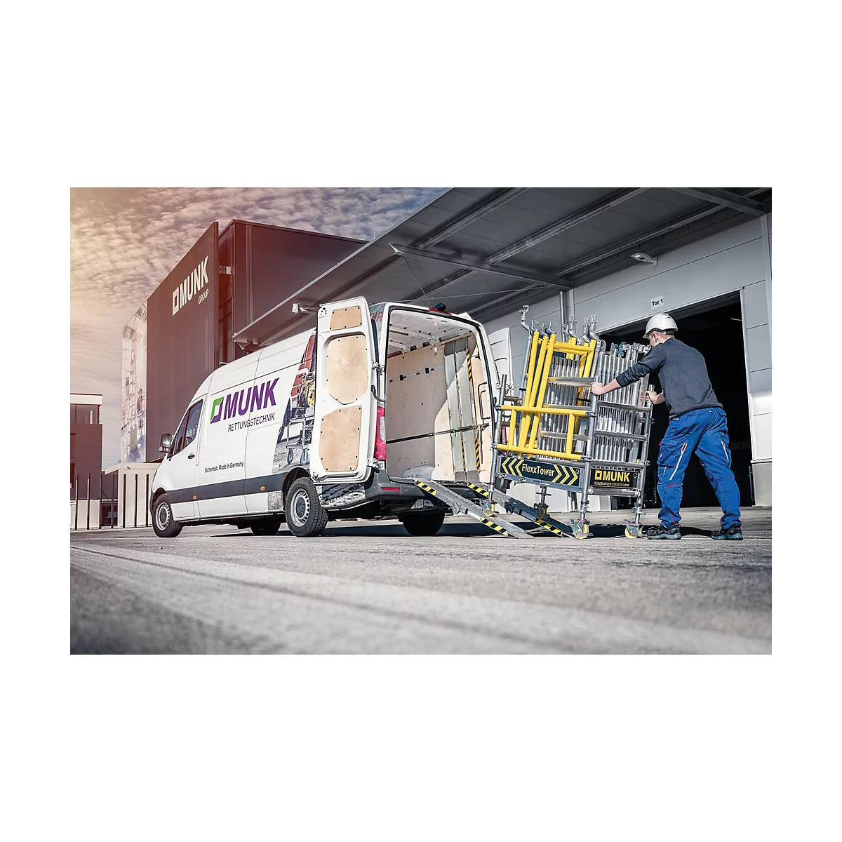Un ouvrier pousse une structure d'échafaudage jaune hors d'une camionnette avec un hayon. Logo et lettrage de l'entreprise sur le véhicule.