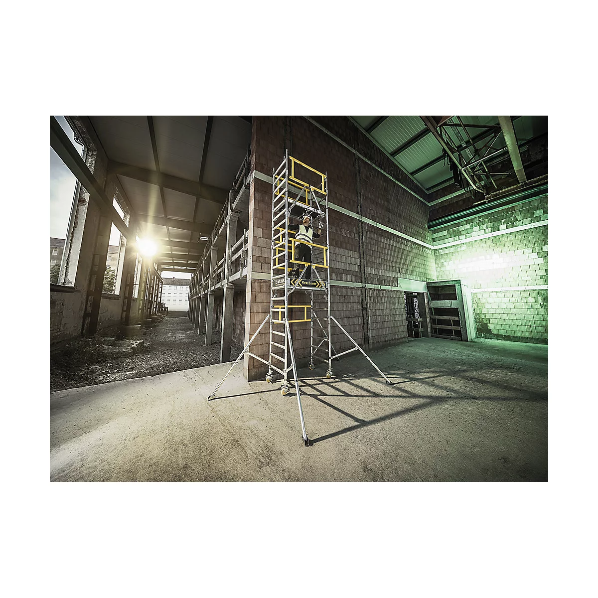 Person auf Gerüst vor Backsteinwand. Arbeitskleidung, gelbe Details, Industriehalle.
