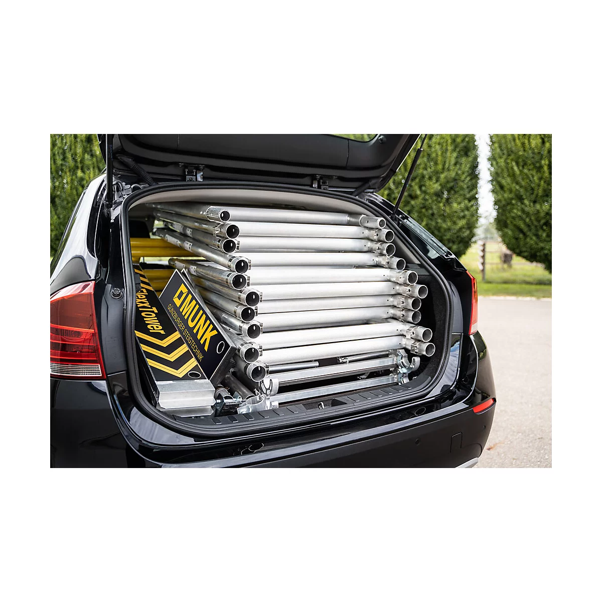 Open trunk of a black car, filled with scaffolding pipes and a toolbox. Box says "MUNK".