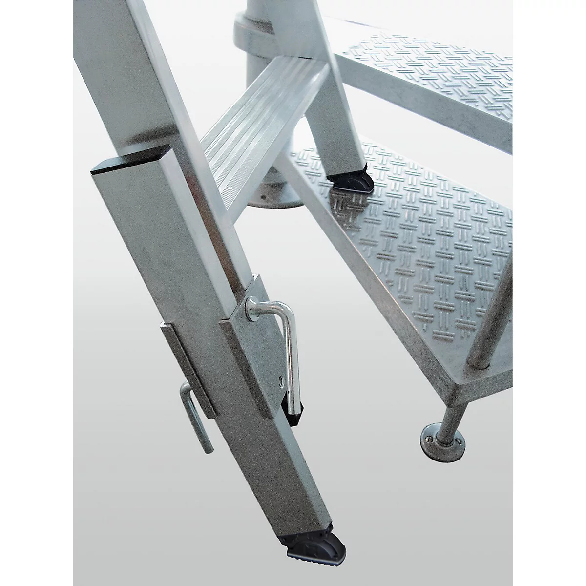 Close-up van een zilveren trap met antislip treden. De ladder heeft zwarte rubberen voetjes en een borgpen.