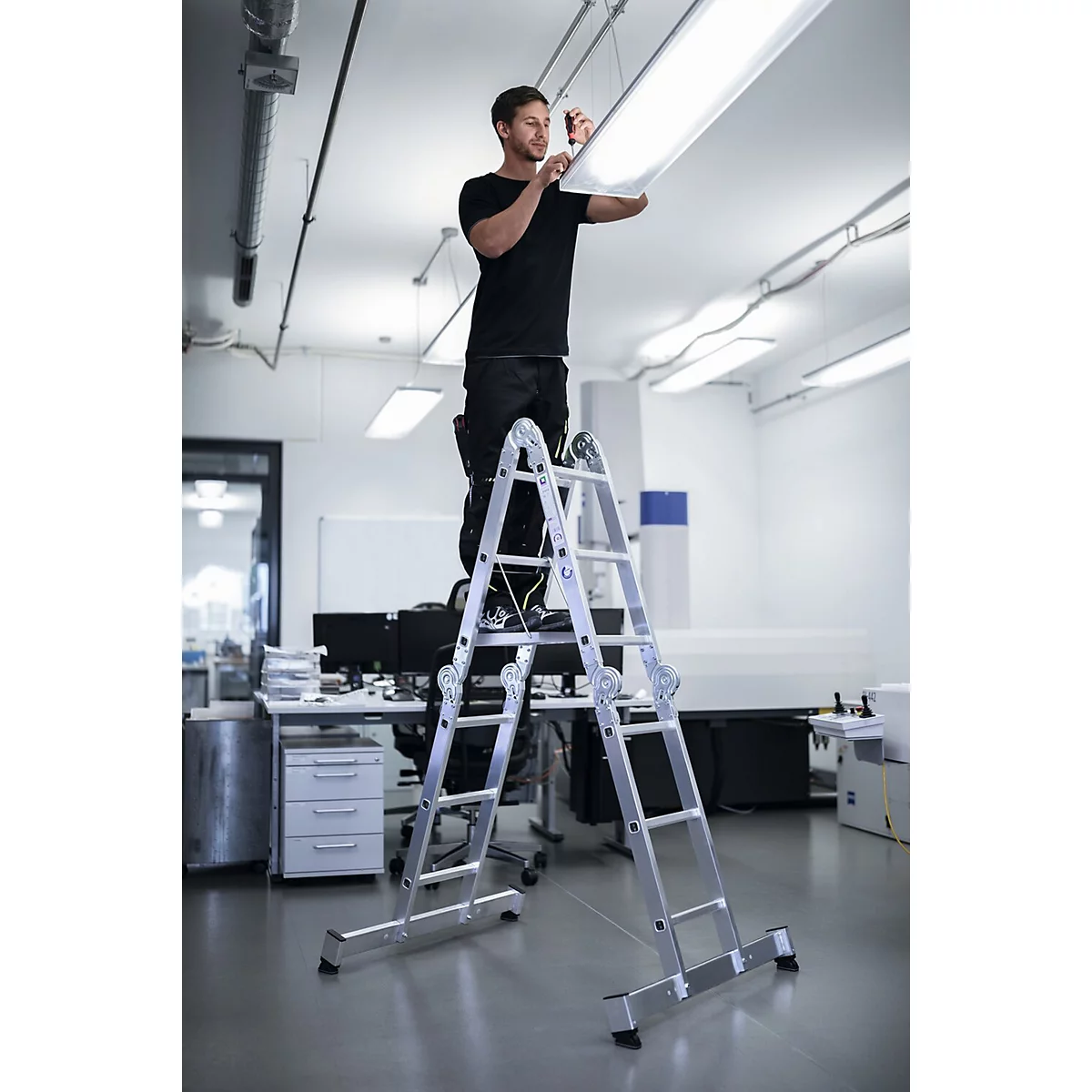 Een man staat op een ladder en installeert een plafondlamp op kantoor.