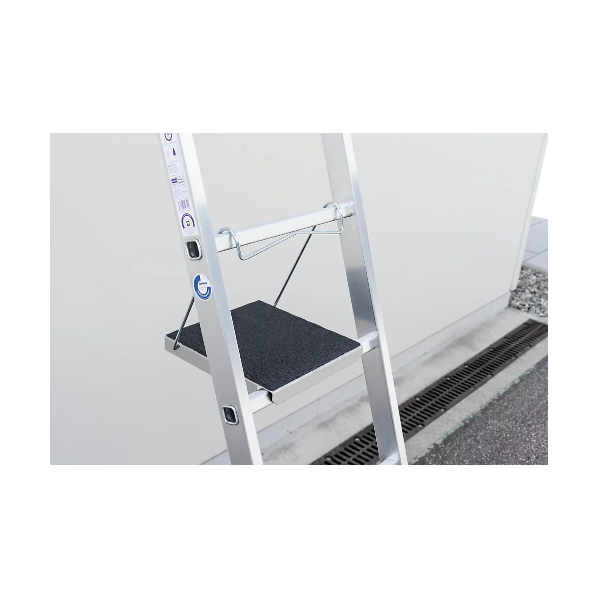 Detailopname van een zilveren trap met een zwarte tree, voor een witte muur.