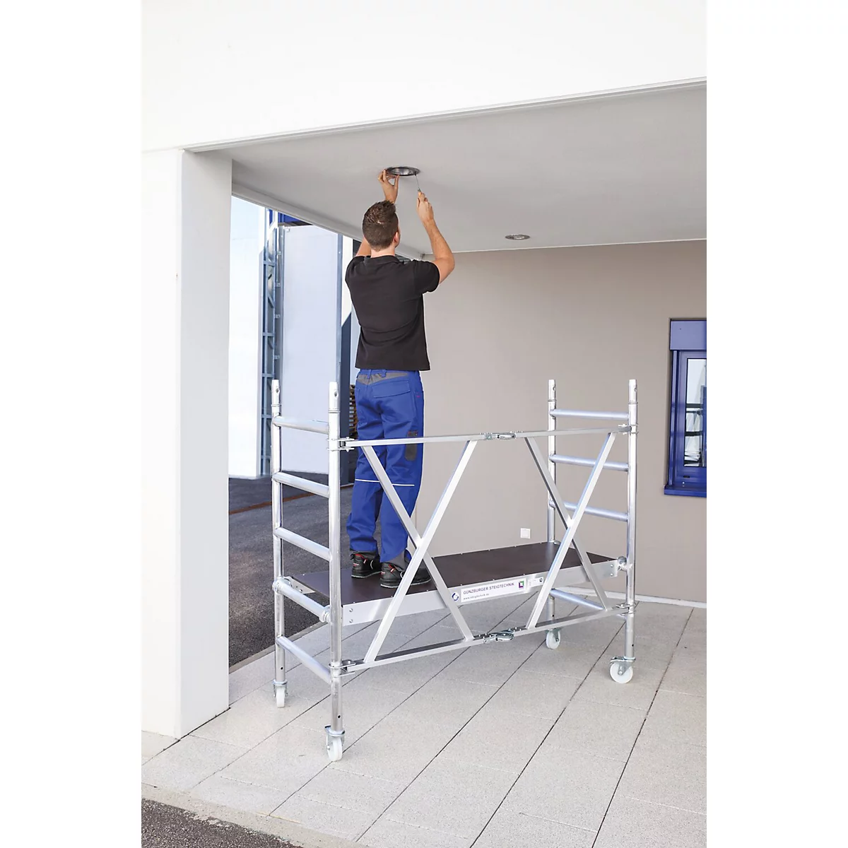A man stands on scaffolding, working on a ceiling light.
