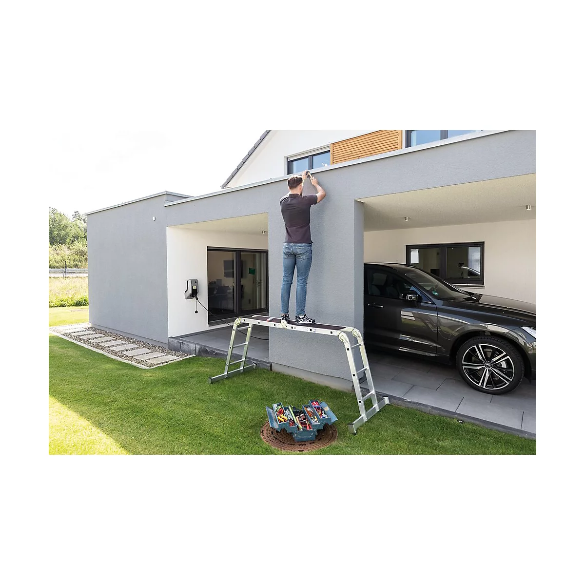 Ein Mann steht auf einer Leiter und arbeitet an der Außenwand eines Hauses. Im Hintergrund ein Auto in der Garage.