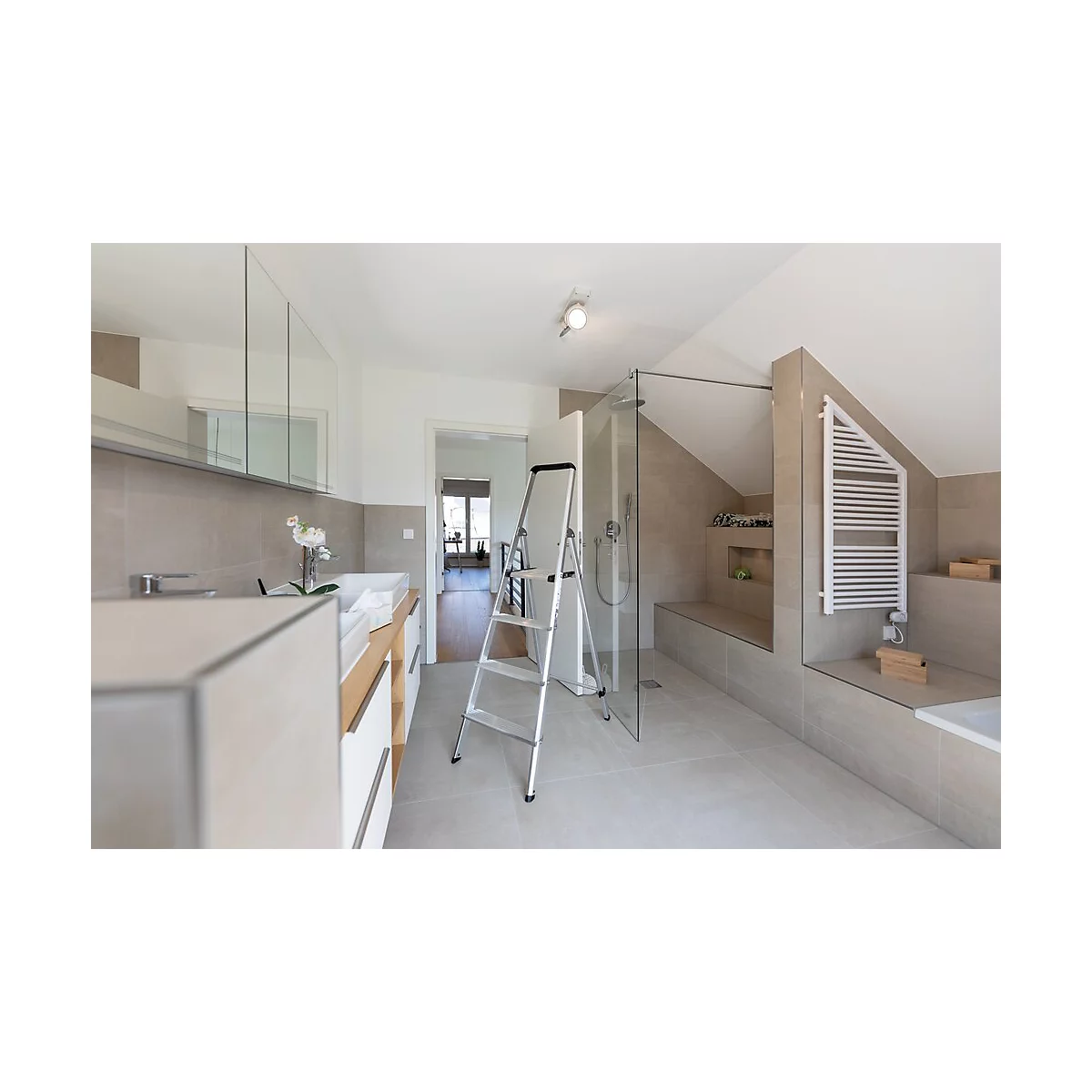 Ruime badkamer met schuine plafonds en moderne meubels. Er staat een ladder in de kamer.