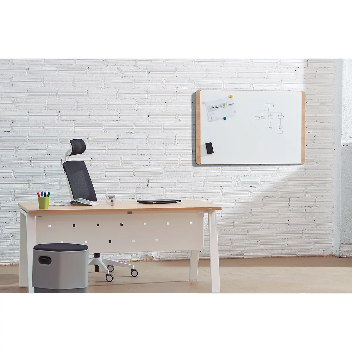 Office with desk, chair, and whiteboard. Laptop and pens on the table. White brick wall.
