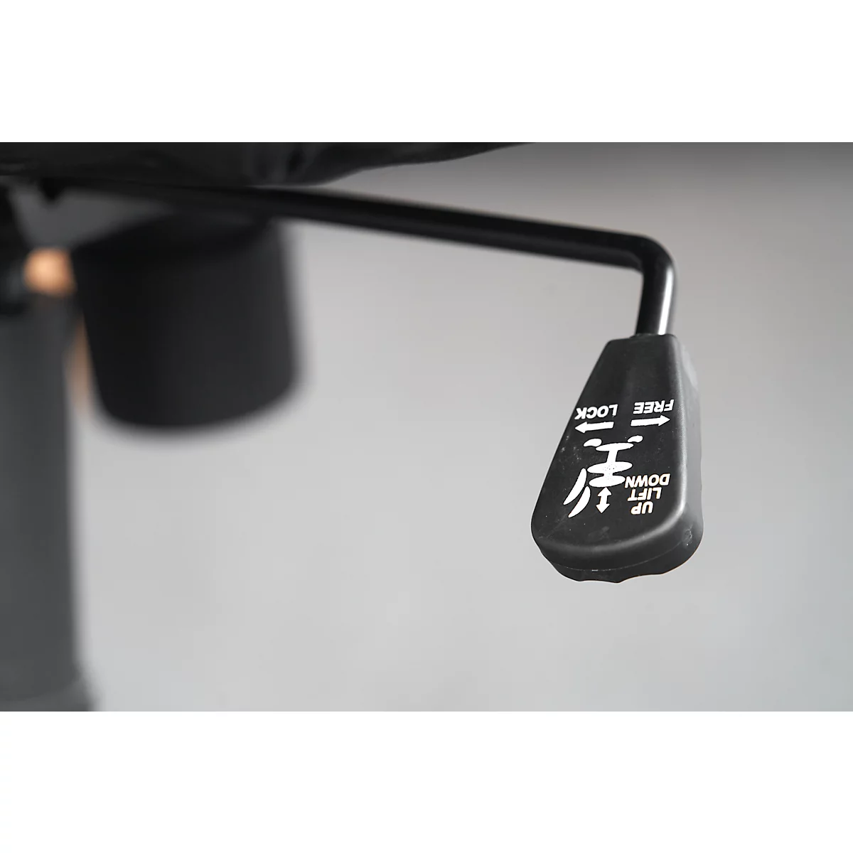 Detail shot of a black lever on an office chair. The lever has white lettering and symbols on it.