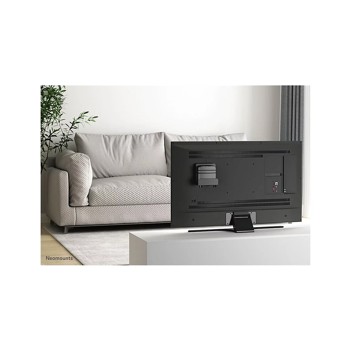 RÃ¼ckseite eines schwarzen Fernsehers, der auf einem weiÃŸen Tisch steht. Im Hintergrund: Couch und Zimmerpflanze.