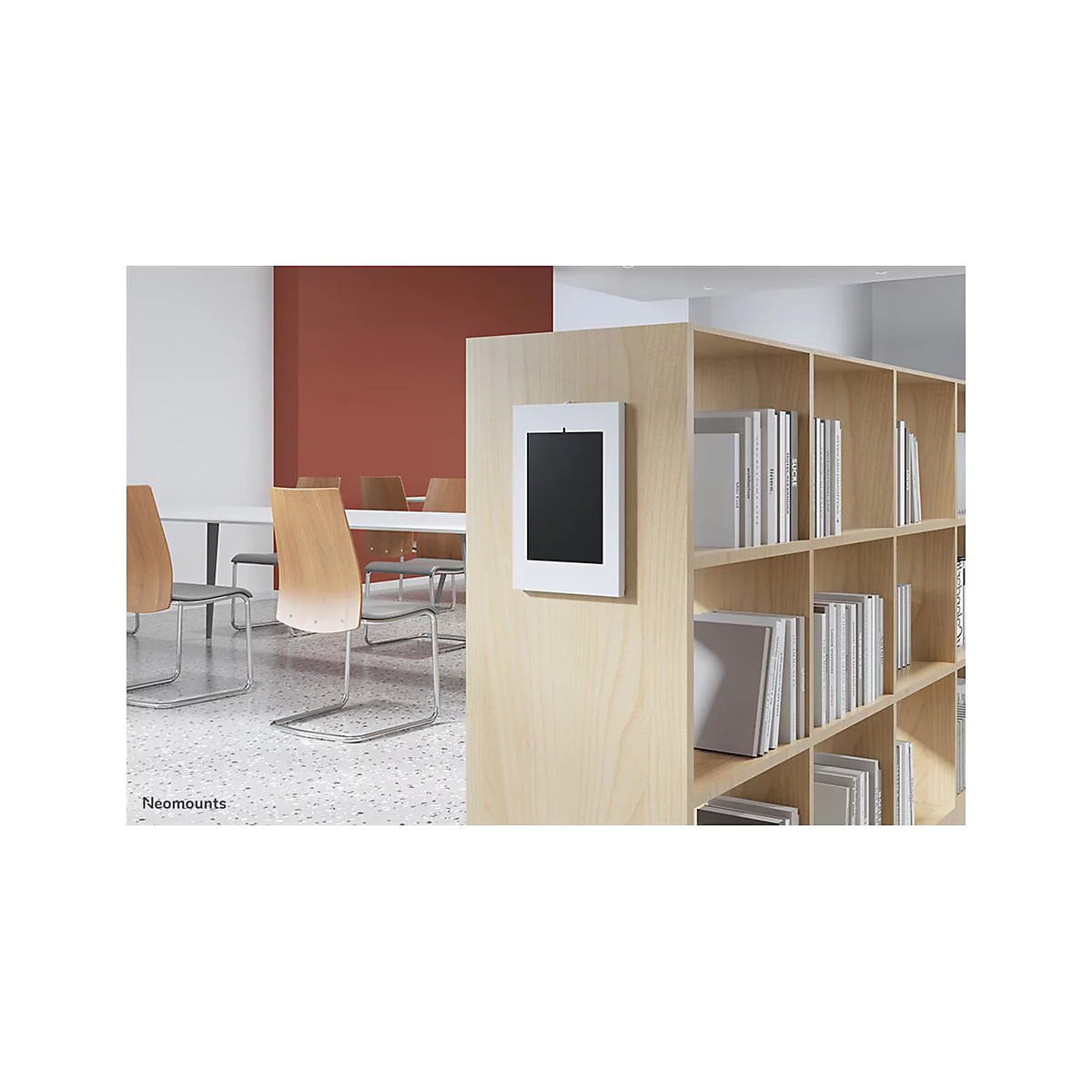 Ein Tablet in weiÃŸem Rahmen an einer hellen Holzwand. Im Hintergrund ein Konferenzraum mit BÃ¼chern.