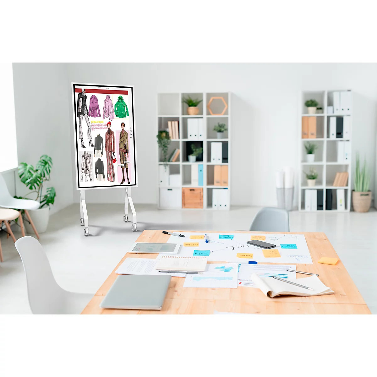 Presentatiebord met modeontwerpen in helder kantoor. Bureau met werkmateriaal, bureaustoelen.