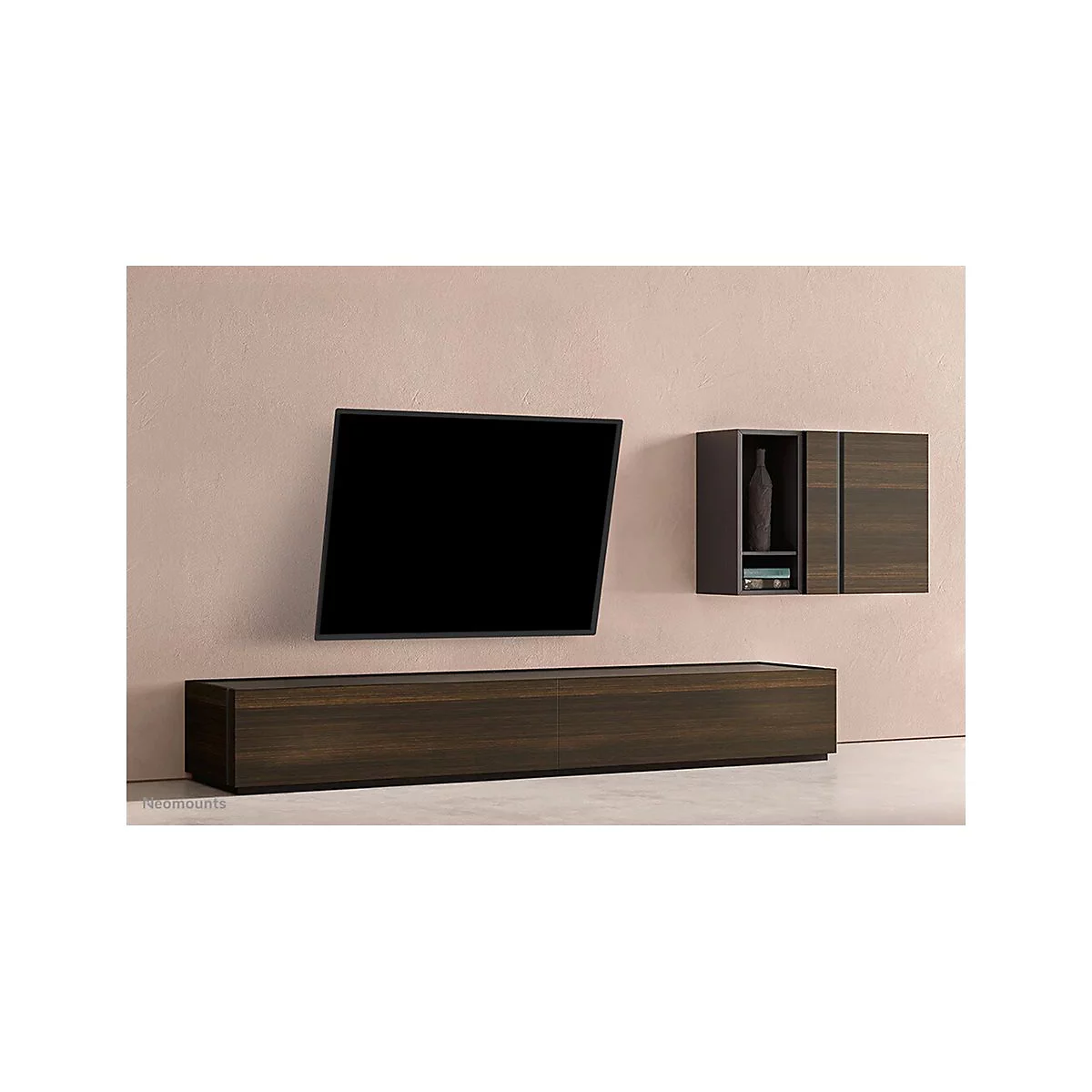 Ein an der Wand montierter Fernseher mit einer darunter liegenden Kommode und einem darüber liegenden Schrank. Alles aus dunklem Holz vor rosa Wand.