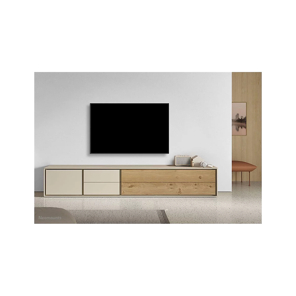 Ein Wohnzimmer mit einem schwarzen Fernseher, der über einer Holzkonsole an der Wand hängt. Auf der Konsole stehen Dekoartikel.