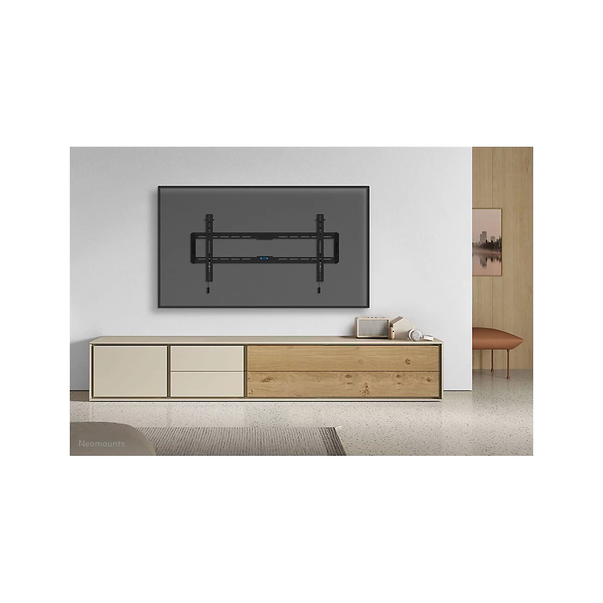 Schwarze TV-Halterung an grauer Wand über Holzschrank. Darunter stehen Lautsprecher, Kopfhörer und Deko.