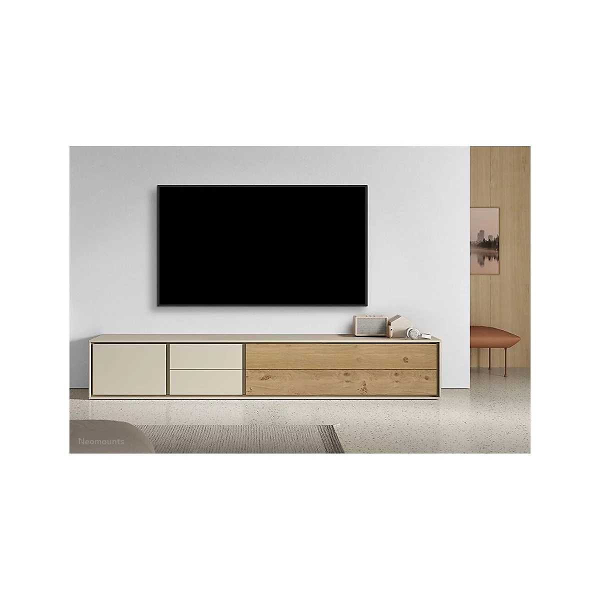 Ein schwarzer Fernseher hängt über einer cremefarbenen und hölzernen TV-Konsole. Auf der Konsole: Lautsprecher, Kopfhörer und Deko.