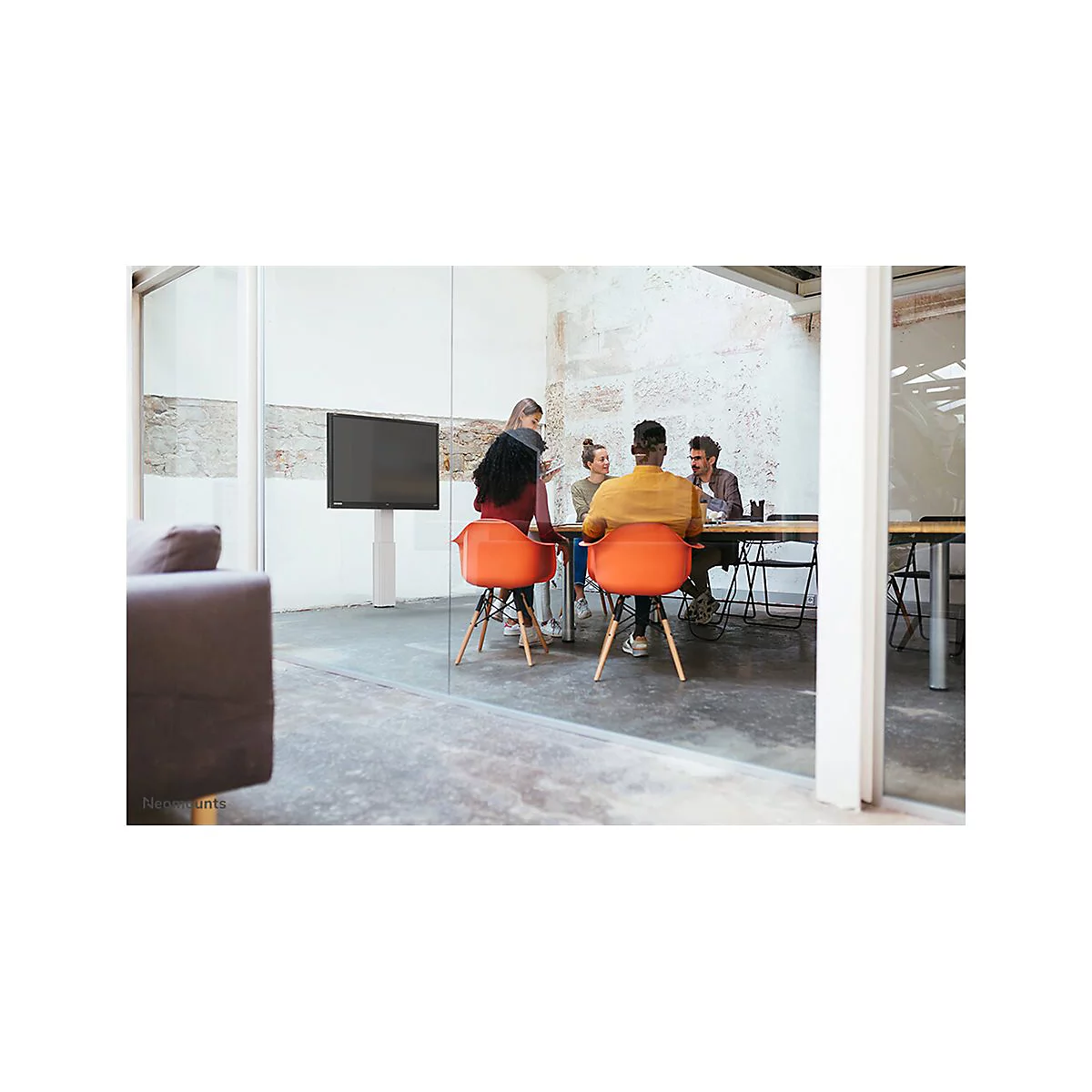 Mehrere Personen sitzen an einem Tisch in einem modernen BÃ¼ro. Orangenfarbene StÃ¼hle und ein groÃŸer Bildschirm.