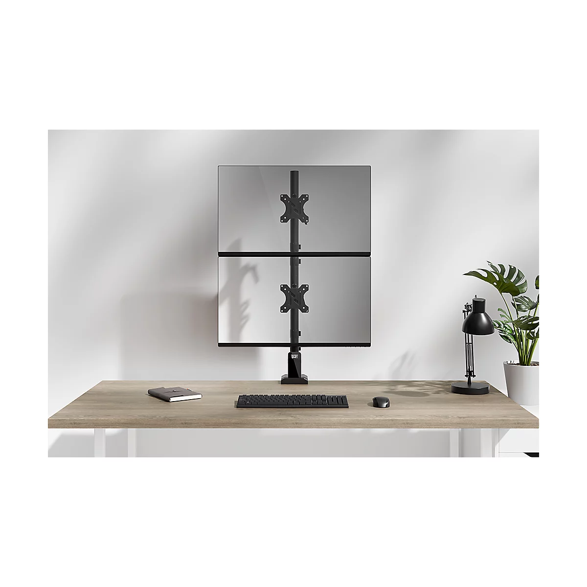 Deux moniteurs montés sur un support noir sont placés sur un bureau en bois. Clavier, souris et bloc-notes sont sur le bureau.