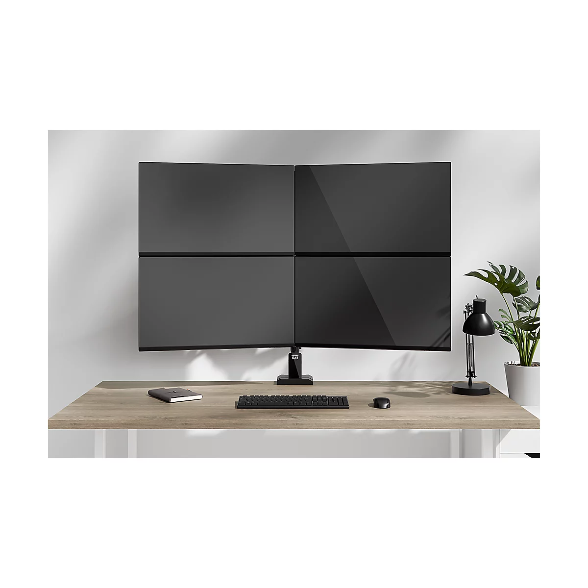 Multi-scherm setup met vier zwarte monitoren boven een bureau. Toetsenbord, muis en notitieblok liggen op het bureau.