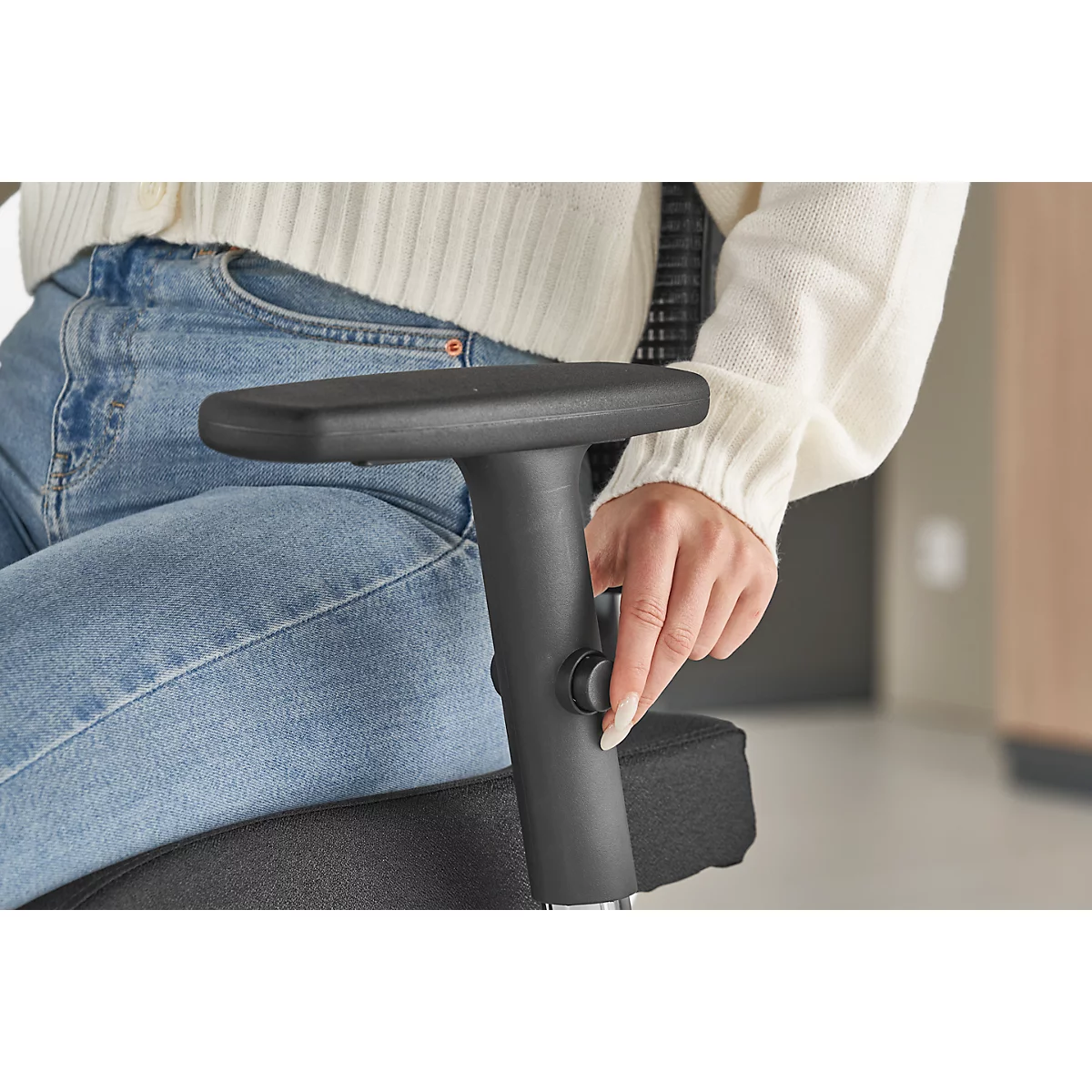 A person adjusting the armrest of a black office chair. The focus is on the hand turning a knob.