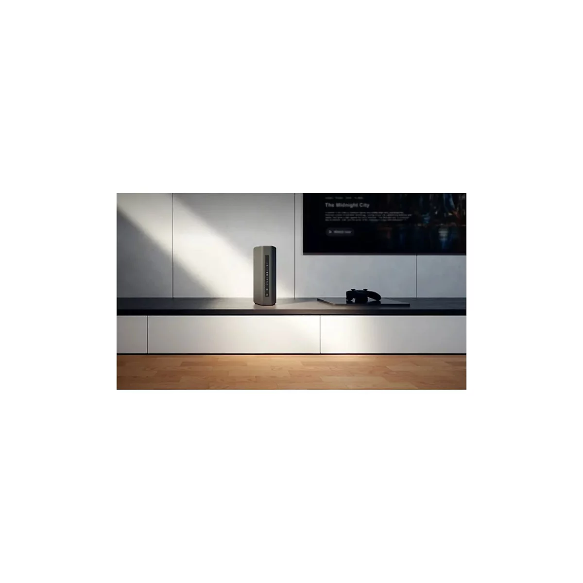 Ein grauer Lautsprecher steht auf einem Regal vor einer Wand mit einem Fernseher und einem Controller.