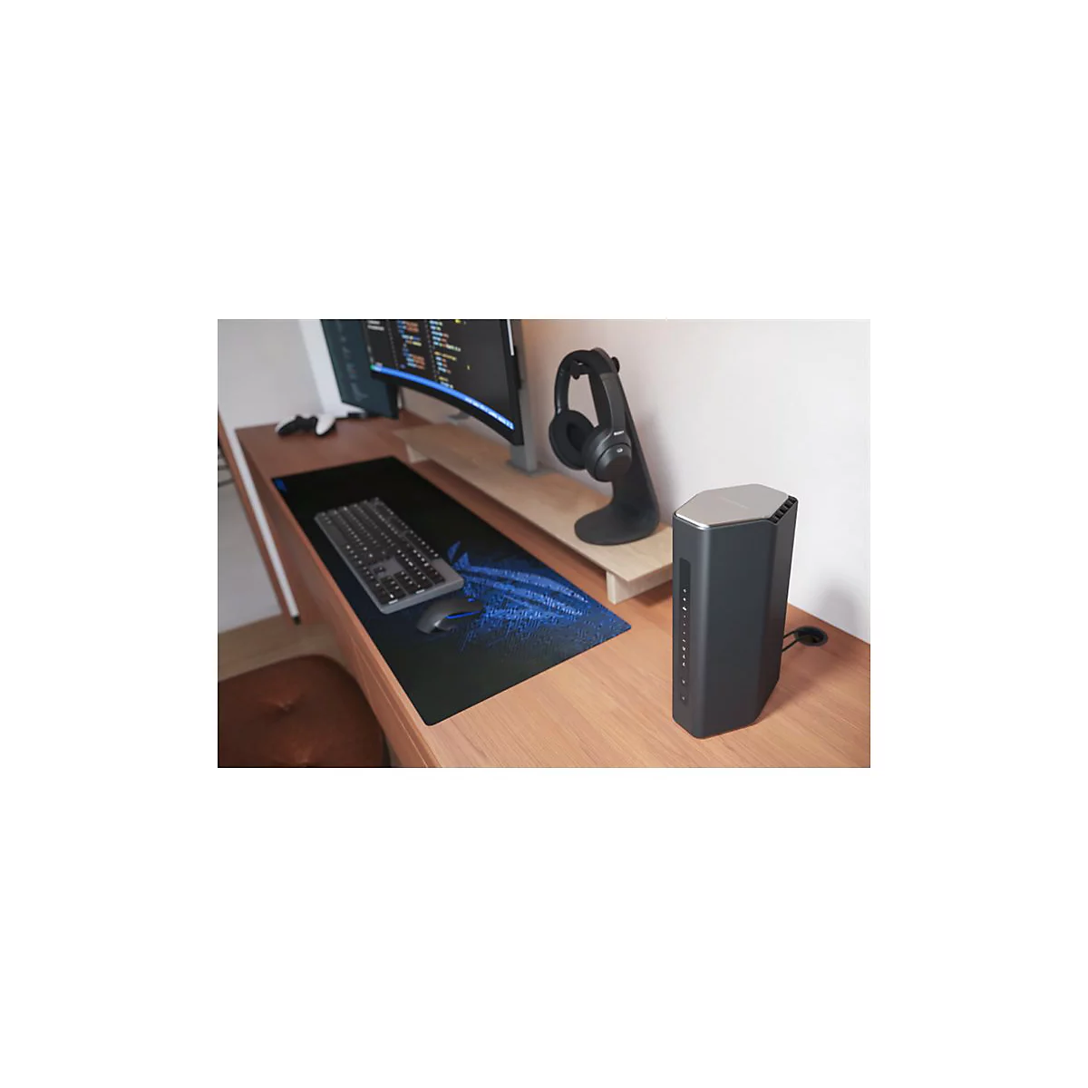 Schreibtisch mit Monitor, Tastatur, Maus, Router und KopfhÃ¶rer. HolzoberflÃ¤che mit blauer Gaming-Mausunterlage.
