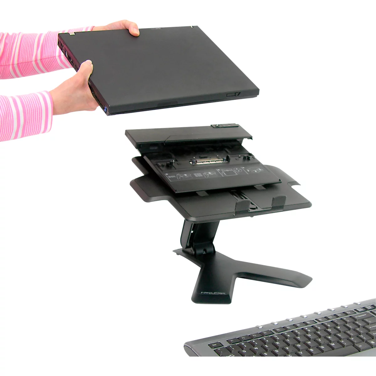 Des mains tiennent un ordinateur portable au-dessus d'une station d'accueil noire, clavier en arrière-plan.