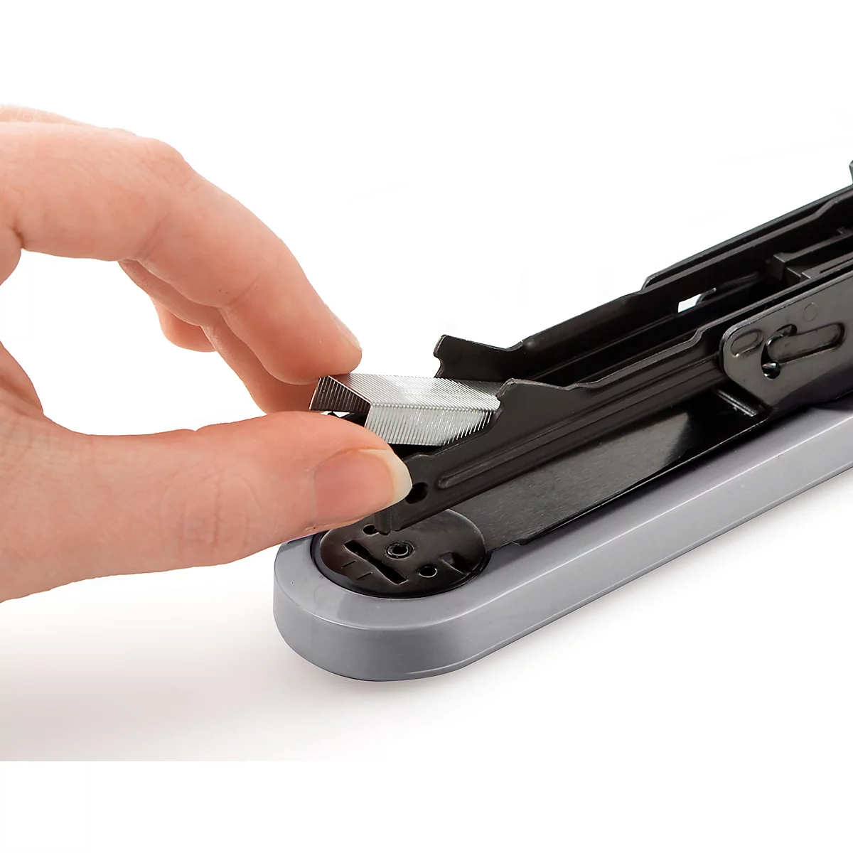 Close-up of a hand inserting staples into a stapler. The stapler has a grey base and a black top.