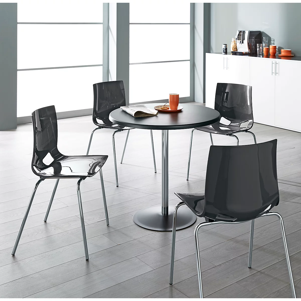 Vier Stühle um einen runden Tisch in modernem Design. Der Tisch ist mit Kaffee und Snacks gedeckt.