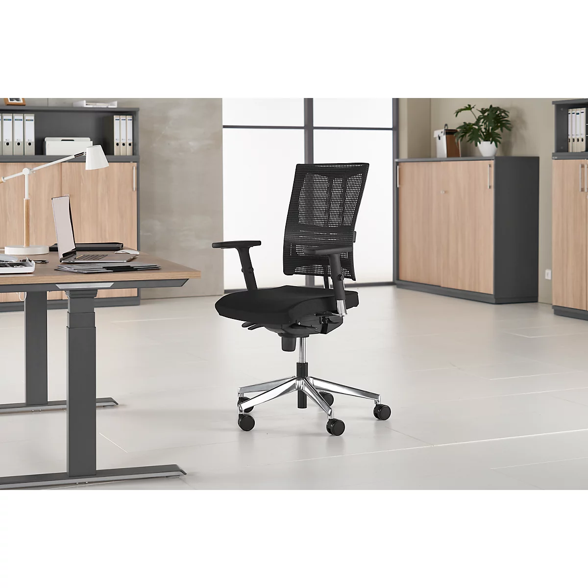 Schwarzer Bürostuhl in modernem Büro. Der Stuhl hat ein Netz-Rückenteil, Armlehnen und ein silbernes Untergestell.