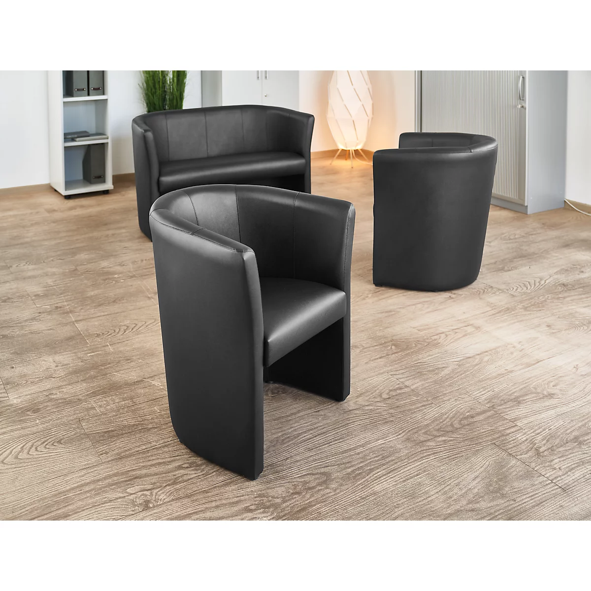 Schwarze Ledersessel und Sofa in einem Wartezimmer. Helles Holzparkett, helle Wände und eine Stehlampe im Hintergrund.