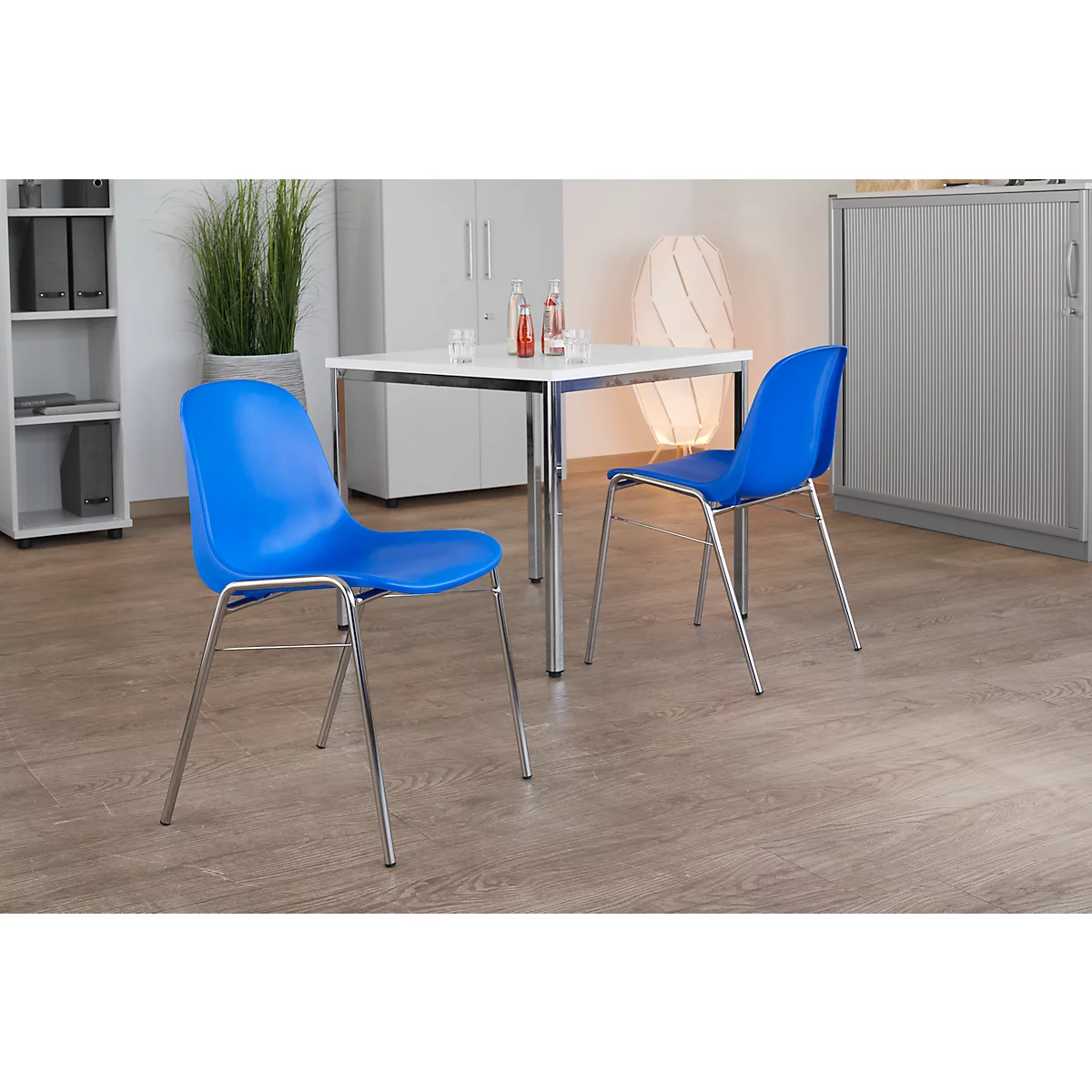 Zwei blaue Stühle stehen an einem weißen Tisch. Die Stuhlbeine sind silberfarben.