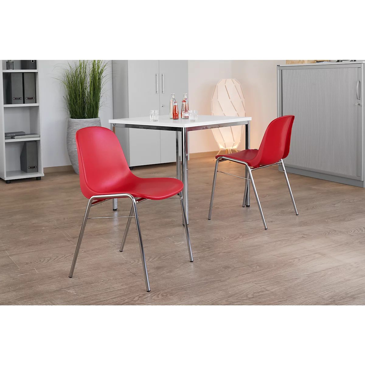 Zwei rote Stühle mit Chromgestell vor einem Tisch. Auf dem Tisch stehen Gläser und Flaschen.