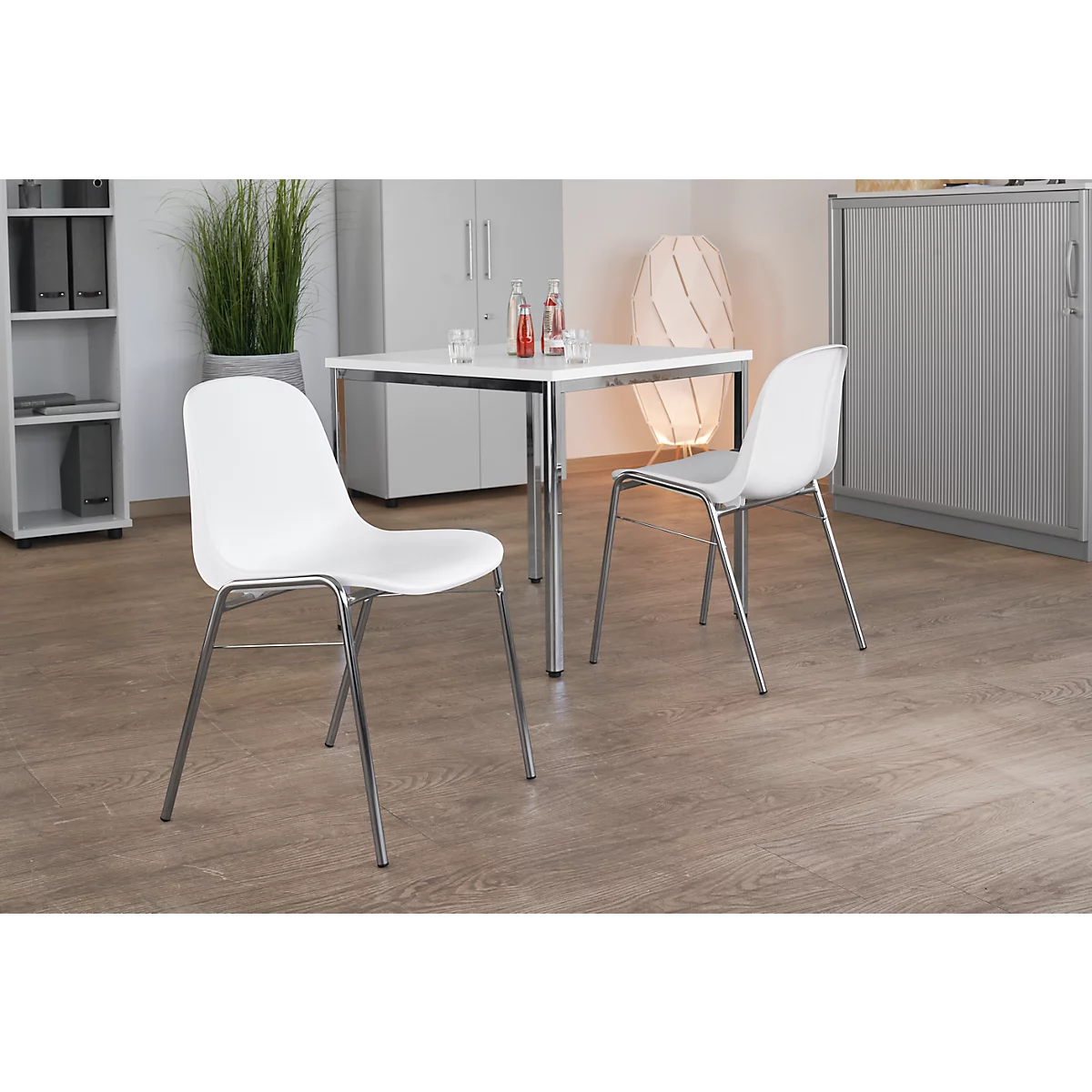 Zwei weiße Stühle mit Metallbeinen vor einem Tisch. Ein minimalistisches Interieur.