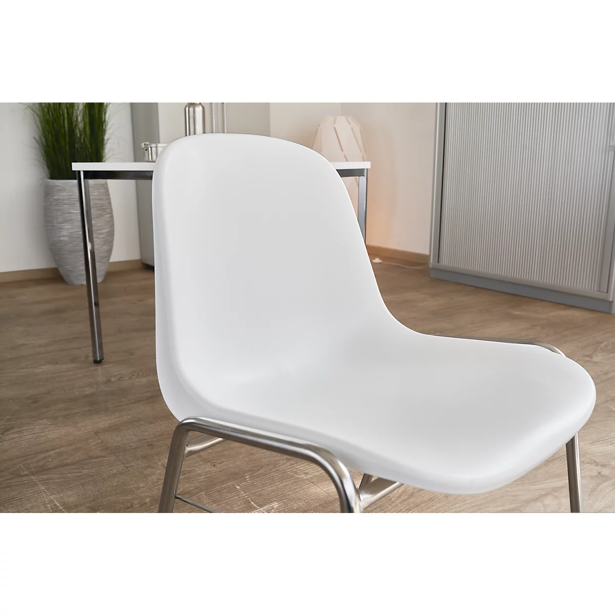Weißer Stuhl mit Metallgestell, im Hintergrund Tisch und Dekoration.