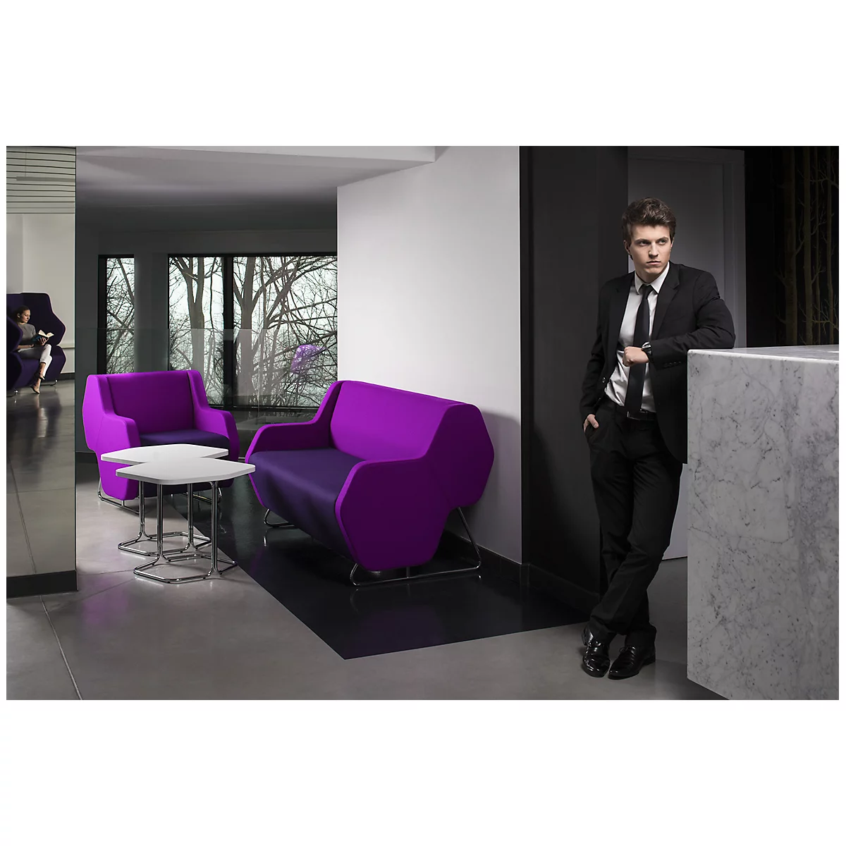 Ein Mann in Anzug lehnt an einer Theke; dahinter violette Designermöbel in modernem Ambiente.