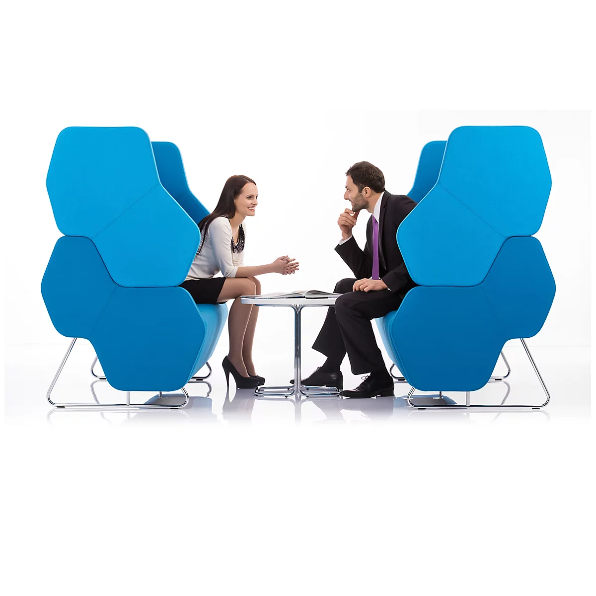 Zwei Personen sitzen in blauen Sesseln und unterhalten sich an einem kleinen Tisch.