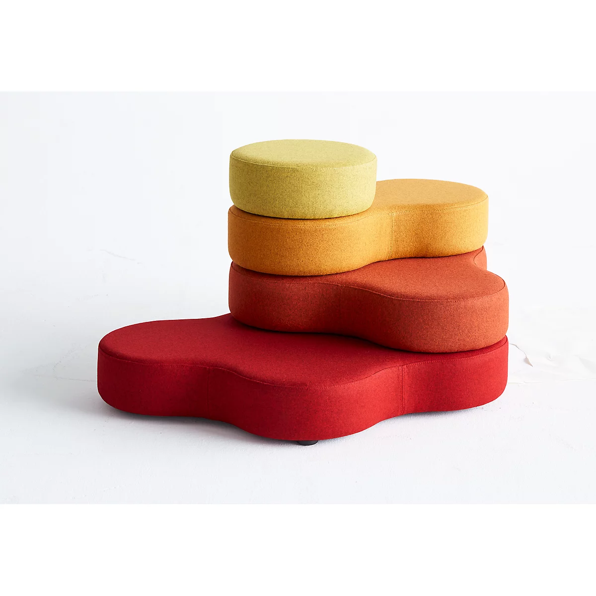 Vierfarbiges Sitzmöbel. Rot unten, orange, rotorange und gelb oben. Alle Teile sind aus Stoff und haben abgerundete Formen.