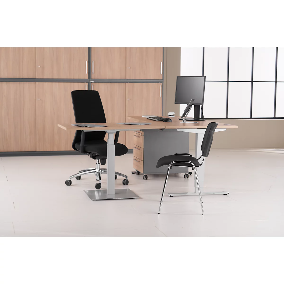 Büro mit Schreibtisch, Stühlen und Computer. Hintergrund: Schrankwand und Fenster.