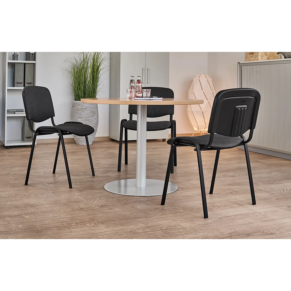 Drei Stühle um einen runden Tisch im Büro. Der Tisch hat eine Holzplatte, die Stühle sind schwarz.