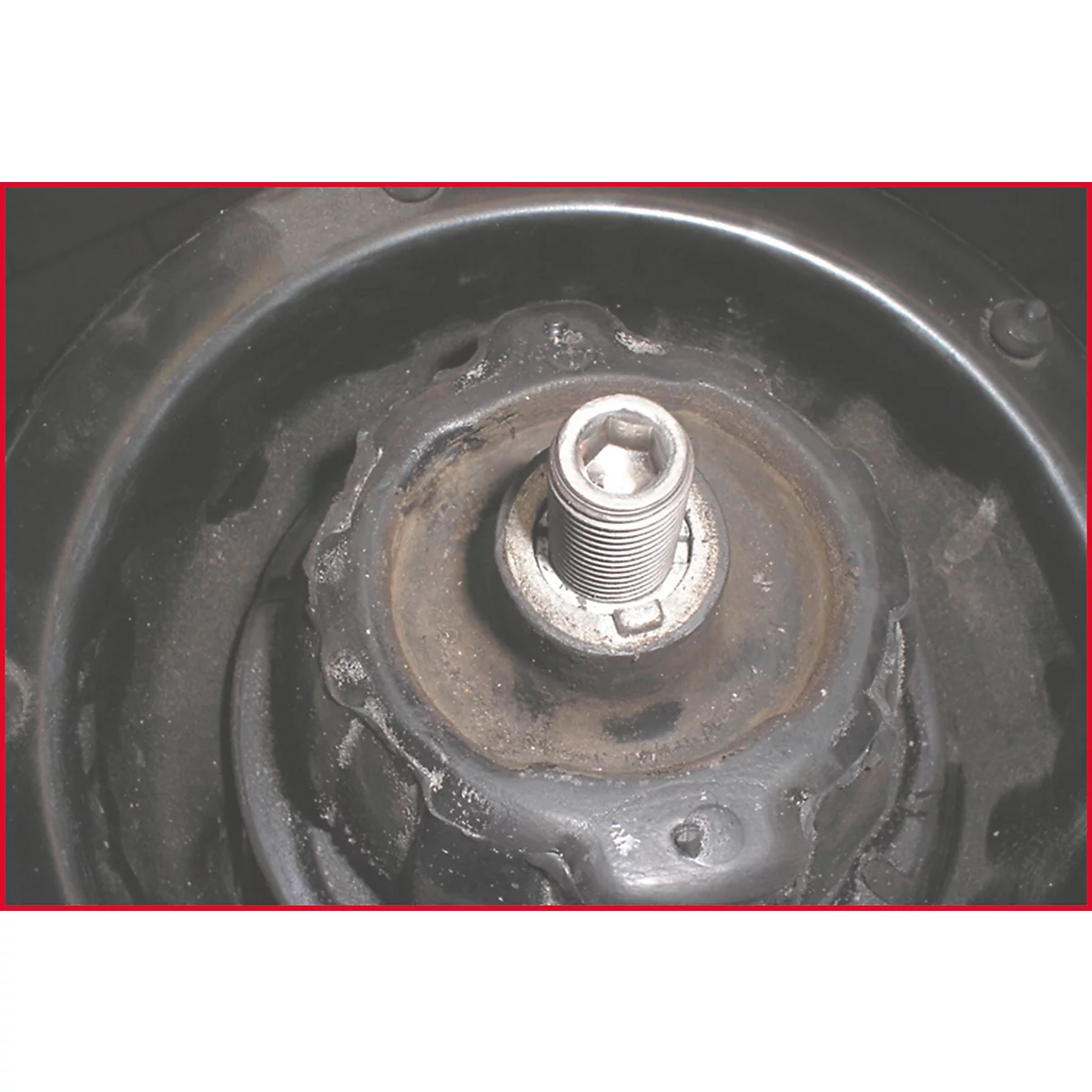 Nahaufnahme einer Fahrzeugaufhängung. Ein Schraubbolzen steht im Mittelpunkt, umgeben von Metallteilen, die auf Abnutzung hindeuten.